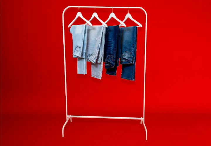 Een wit kledingrek met vier blauwe spijkerbroeken die hangen tegen een felrode achtergrond.